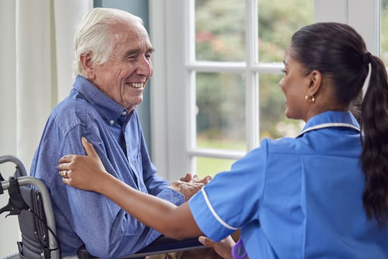 Care worker talking with senior man sitting in wheelchair in care home